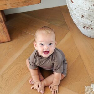 A baby is sitting on a Zimmi Onesie - Tort floor.